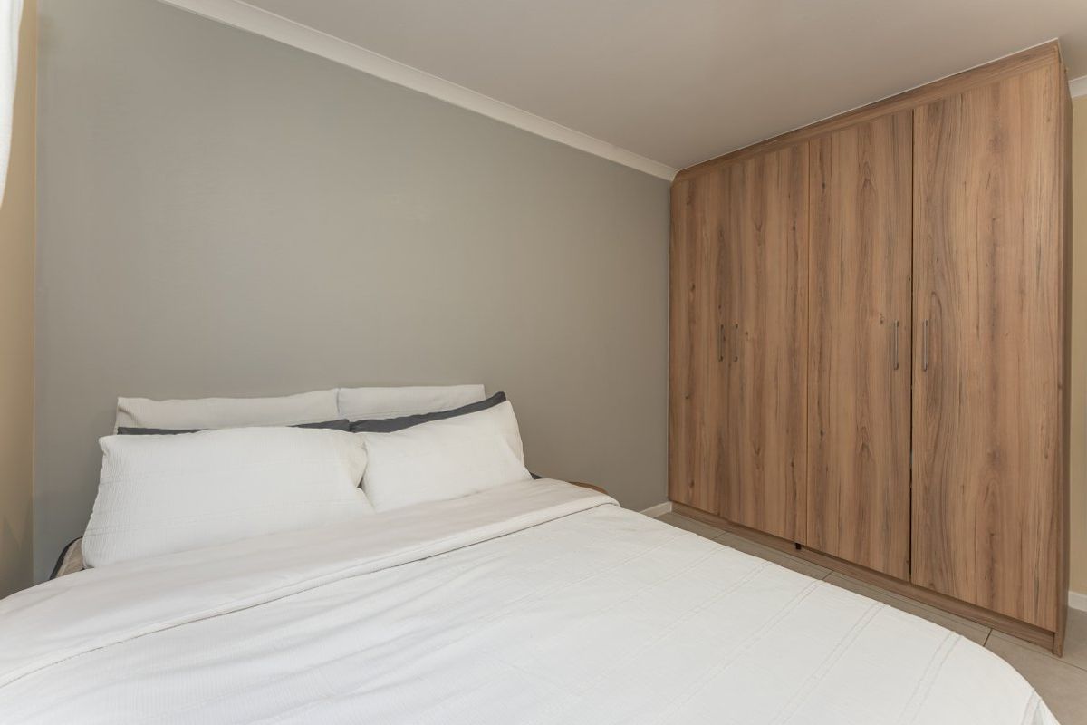 A well-maintained bedroom featuring neutral wall tones and floor-to-ceiling built-in wooden cupboards providing ample storage space.
