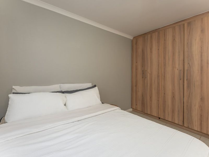 A well-maintained bedroom featuring neutral wall tones and floor-to-ceiling built-in wooden cupboards providing ample storage space.