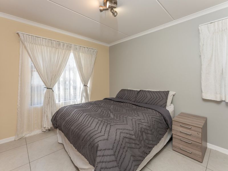 A functional bedroom featuring tiled flooring, a built-in wardrobe, and neutral wall tones, providing a clean and practical living space.