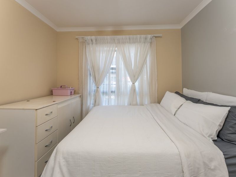 A standard bedroom featuring neutral wall tones, coving, and a window with sheer curtains, providing a functional and well-lit sleeping space.