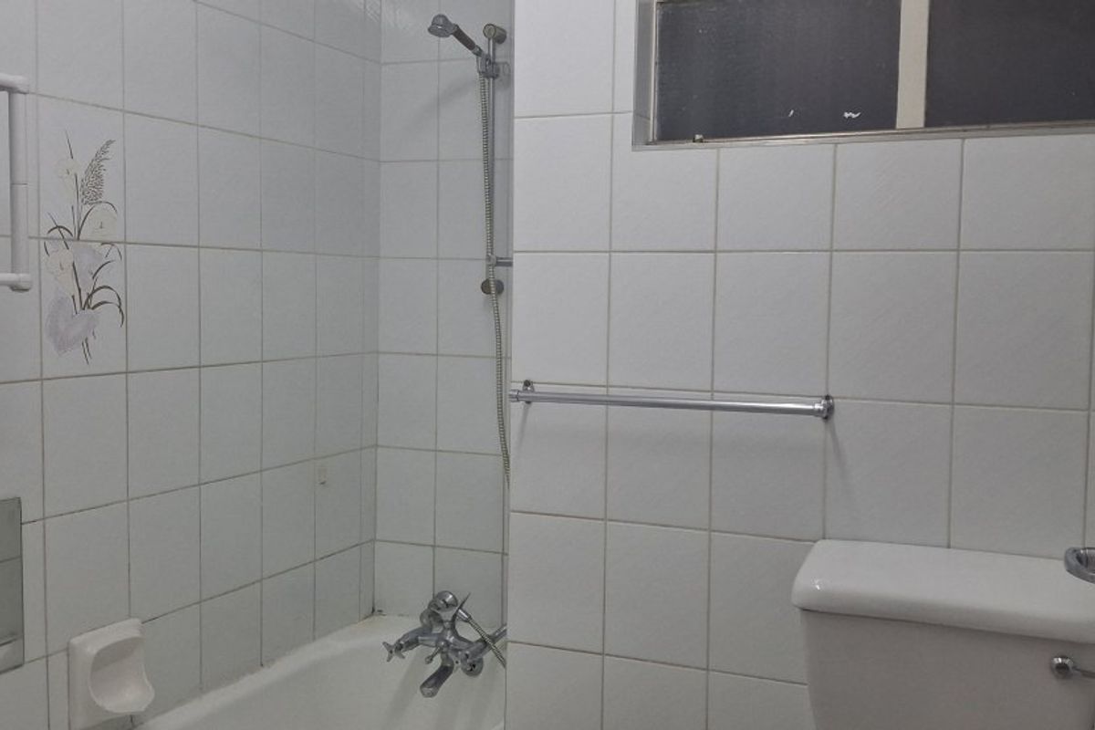 A functional bathroom featuring a bathtub with shower mixer, white wall tiles, and a standard toilet, requiring cosmetic updates to modernize the space.