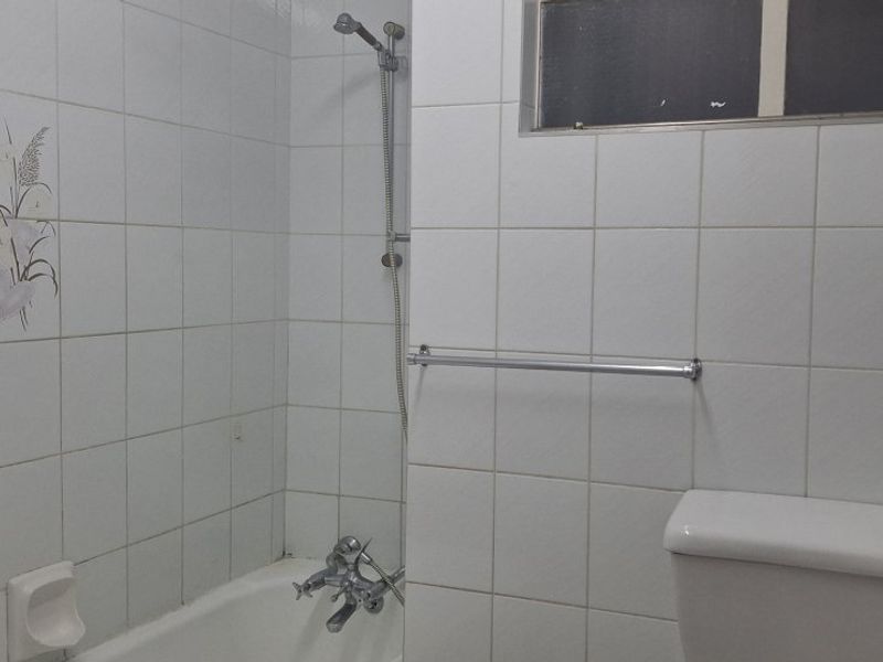 A functional bathroom featuring a bathtub with shower mixer, white wall tiles, and a standard toilet, requiring cosmetic updates to modernize the space.