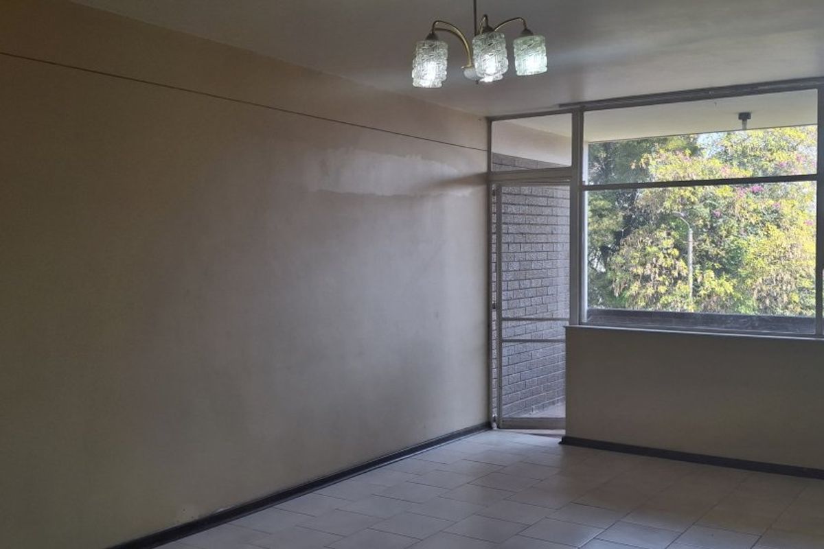 An empty living room featuring tiled flooring, a large window with natural light, and a brick feature wall.