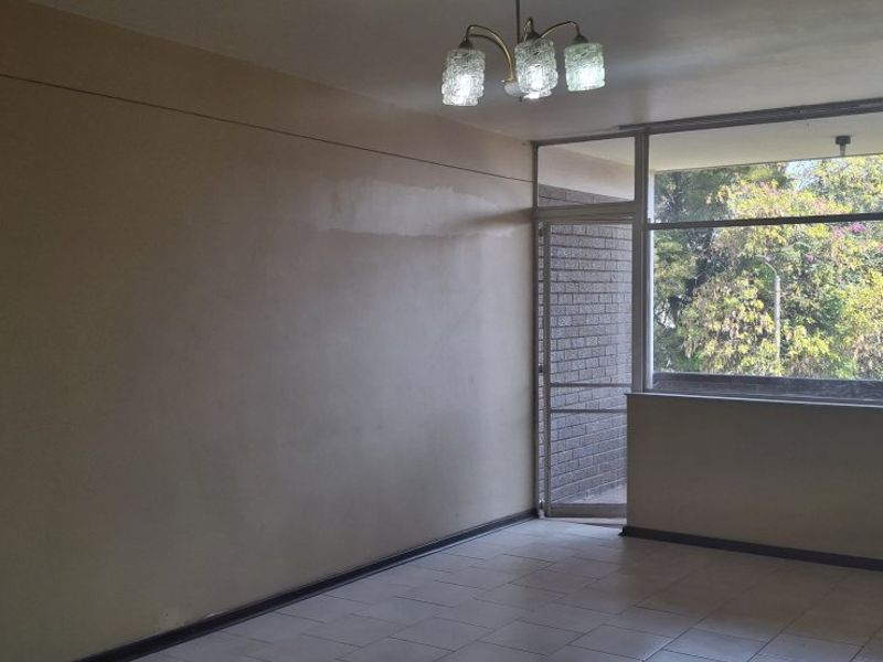 An empty living room featuring tiled flooring, a large window with natural light, and a brick feature wall.