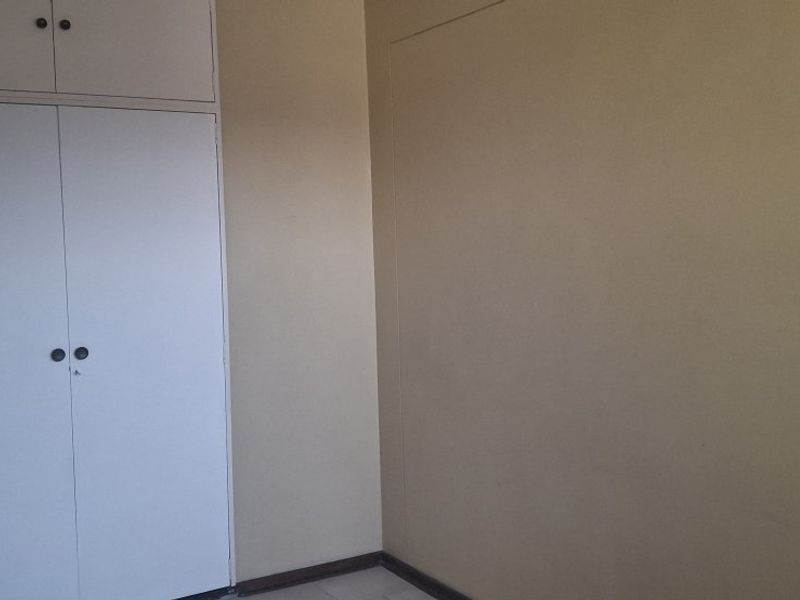 An empty bedroom featuring built-in cupboards with overhead storage, neutral wall tones, and tiled flooring.
