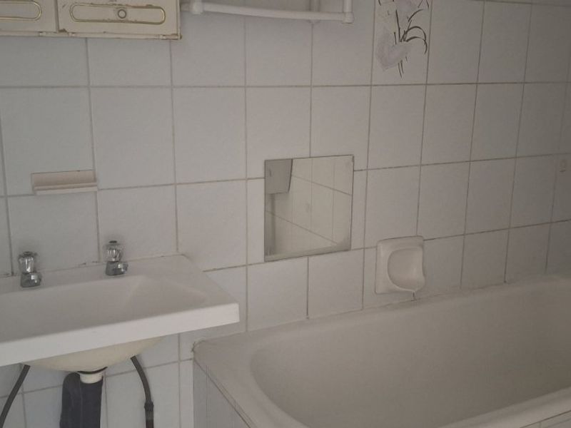 A dated bathroom featuring a wall-mounted basin, built-in bathtub, and white wall tiling, offering potential for a modern renovation.