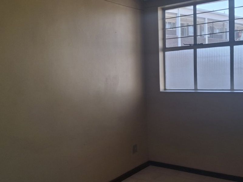 An empty bedroom featuring tiled flooring, a steel-framed window with security bars, and neutral wall finishes.
