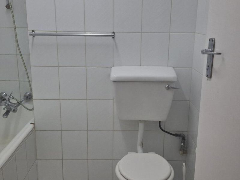 A compact bathroom featuring a standard bathtub with shower mixer, a white toilet, and tiled walls. The space is dated and requires cosmetic updates.