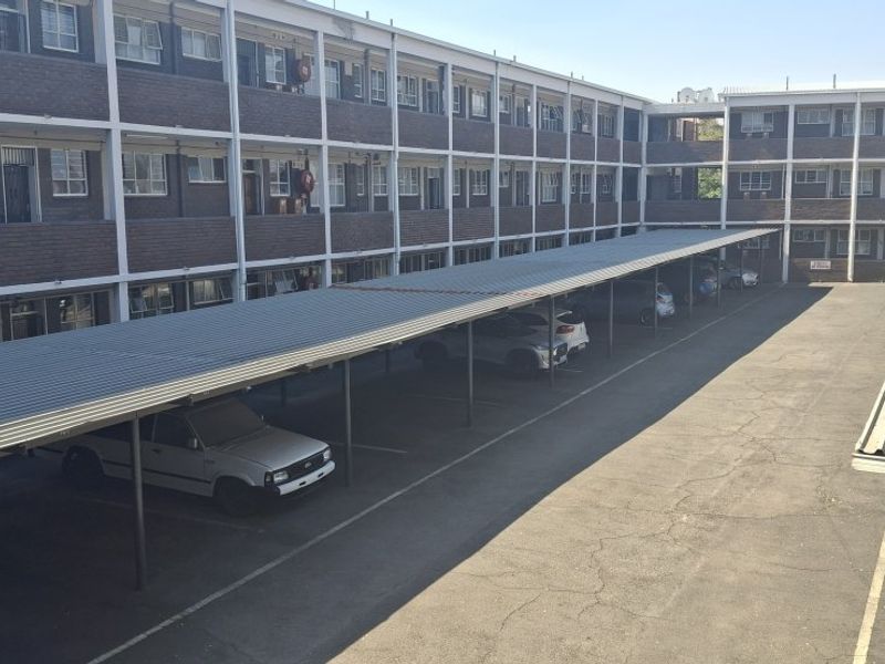 Exterior view of an apartment complex featuring multi-level brick residential units and covered parking bays with asphalt driveway.
