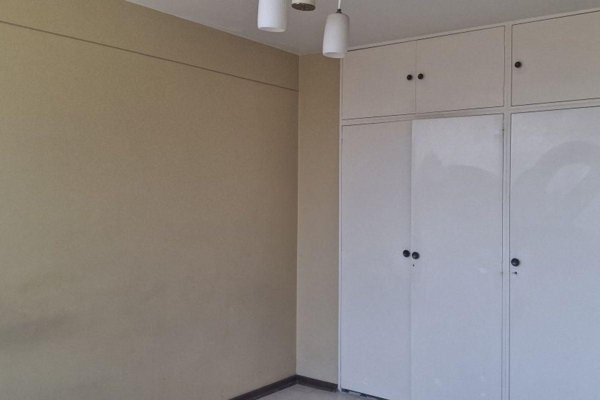 A vacant bedroom featuring built-in cupboards with integrated overhead storage and a simple pendant light fixture.