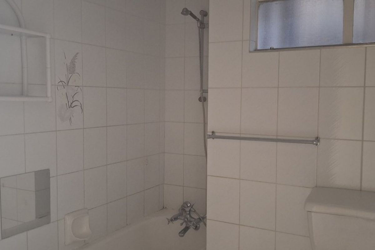 A functional bathroom featuring a bathtub with shower mixer, white wall tiles, and a toilet, presenting an opportunity for modernization.