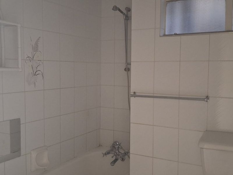A functional bathroom featuring a bathtub with shower mixer, white wall tiles, and a toilet, presenting an opportunity for modernization.