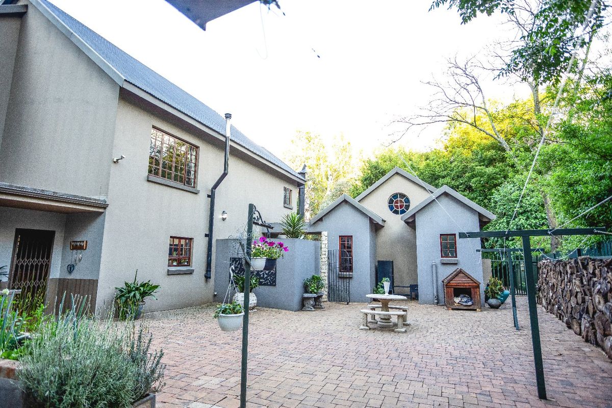 A spacious rear courtyard featuring paved flooring, stone retaining walls, and access to the main residence and secondary structure.