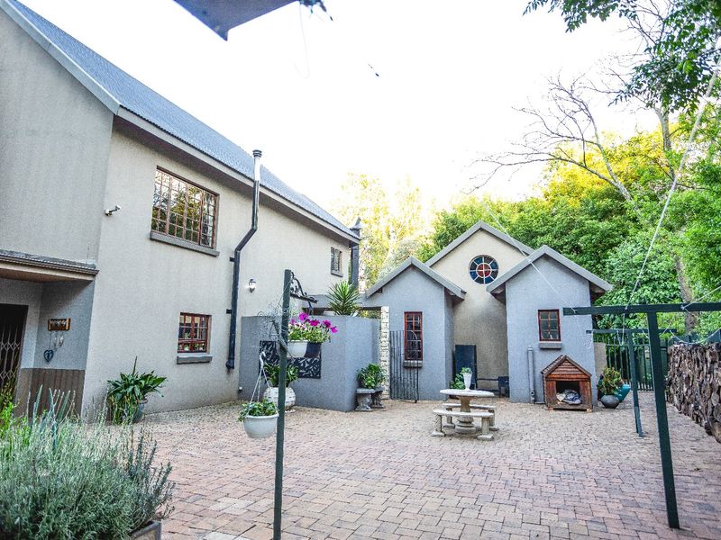 A spacious rear courtyard featuring paved flooring, stone retaining walls, and access to the main residence and secondary structure.