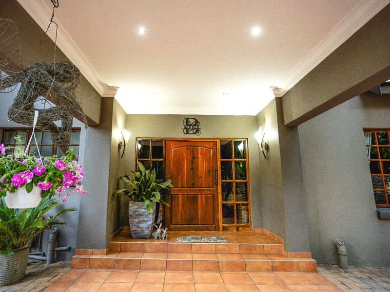 A welcoming covered entrance featuring a solid wood front door, tiled steps, and elegant wall-mounted lighting under a coved ceiling.