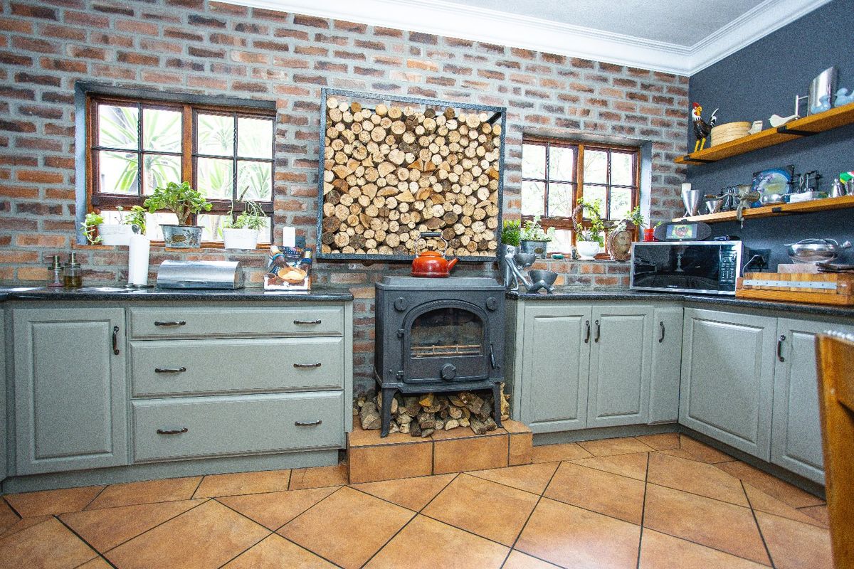 A rustic kitchen featuring exposed brick walls, a central cast iron wood-burning stove, fitted cabinetry with granite countertops, and tiled flooring.