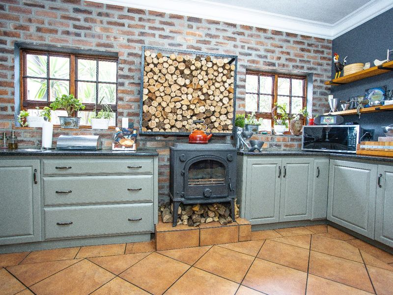 A rustic kitchen featuring exposed brick walls, a central cast iron wood-burning stove, fitted cabinetry with granite countertops, and tiled flooring.