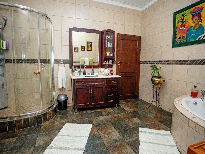 Spacious bathroom featuring a curved glass shower, built-in vanity with storage, and a tiled bathtub surround with neutral wall and floor tiling.