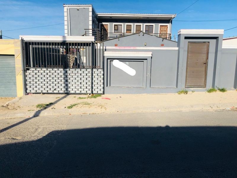 Front exterior view of a two-story house featuring a grey painted facade, secure boundary wall, and metal entrance gate.