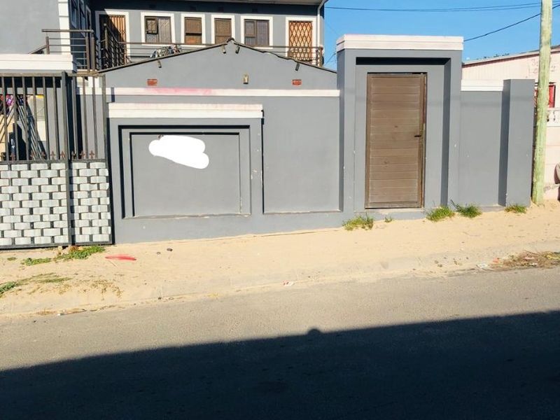 Front exterior view of the property featuring a grey boundary wall, pedestrian entrance gate, and secure perimeter fencing.