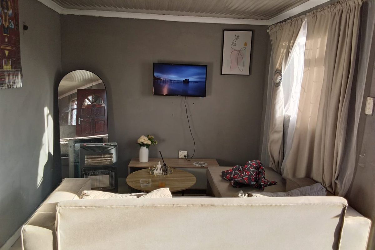 A compact living room featuring grey walls, a window with curtains, and basic electrical fixtures, offering a functional space for relaxation.