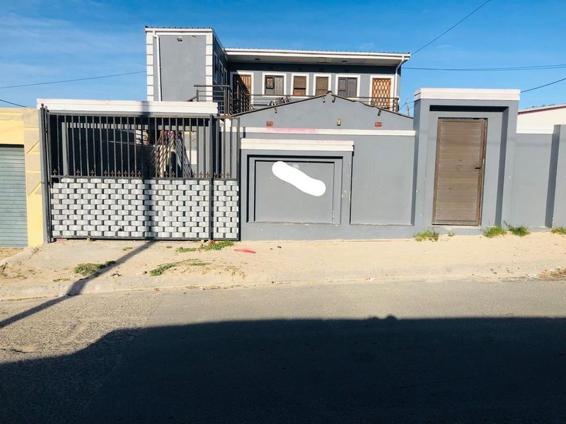 Front elevation of a two-story house featuring a secure perimeter wall, metal gate, and pedestrian entrance.