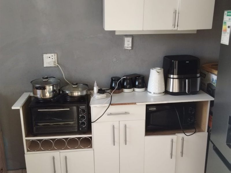 A compact kitchen area featuring white built-in cabinetry and tiled flooring, currently showing signs of wear and unfinished wall surfaces.