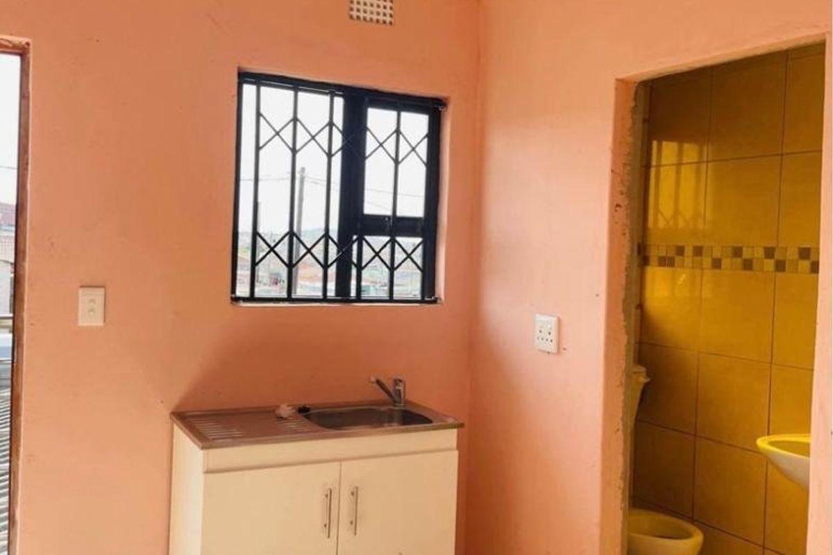 A compact kitchen area featuring a single sink unit, tiled flooring, and an adjacent bathroom, requiring cosmetic updates and finishing touches.