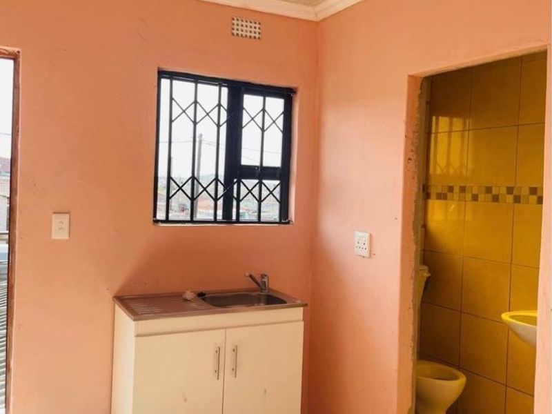 A compact kitchen area featuring a single sink unit, tiled flooring, and an adjacent bathroom, requiring cosmetic updates and finishing touches.