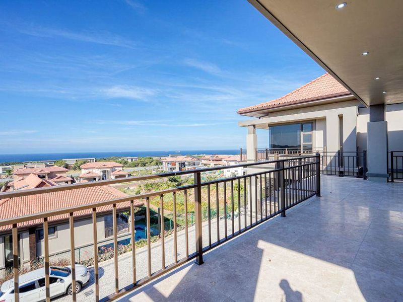 Spacious covered balcony featuring tiled flooring, metal balustrades, and recessed lighting, offering expansive elevated views of the surrounding estate and coastline.