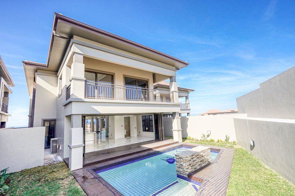 Rear view of a modern townhouse featuring a swimming pool, wooden decking, and a spacious covered balcony accessible via large sliding doors.