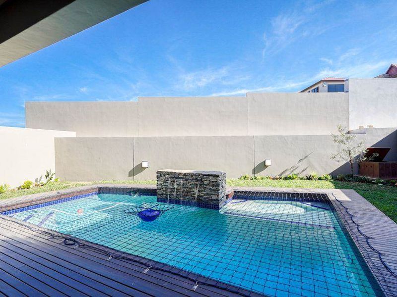 A private backyard pool area featuring a stone water feature, timber decking, and a secure boundary wall, perfect for outdoor relaxation.