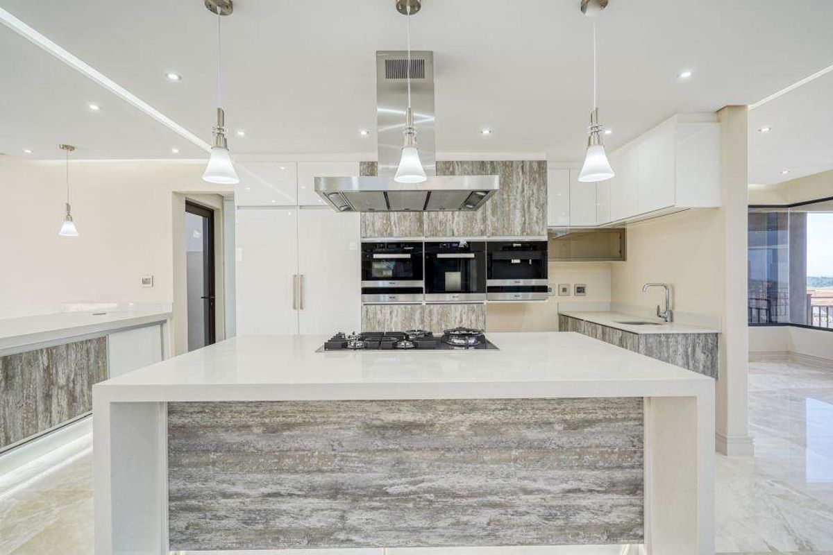 Modern kitchen featuring a large central island with a gas hob, integrated appliances, stone countertops, and sleek cabinetry with recessed and pendant lighting.
