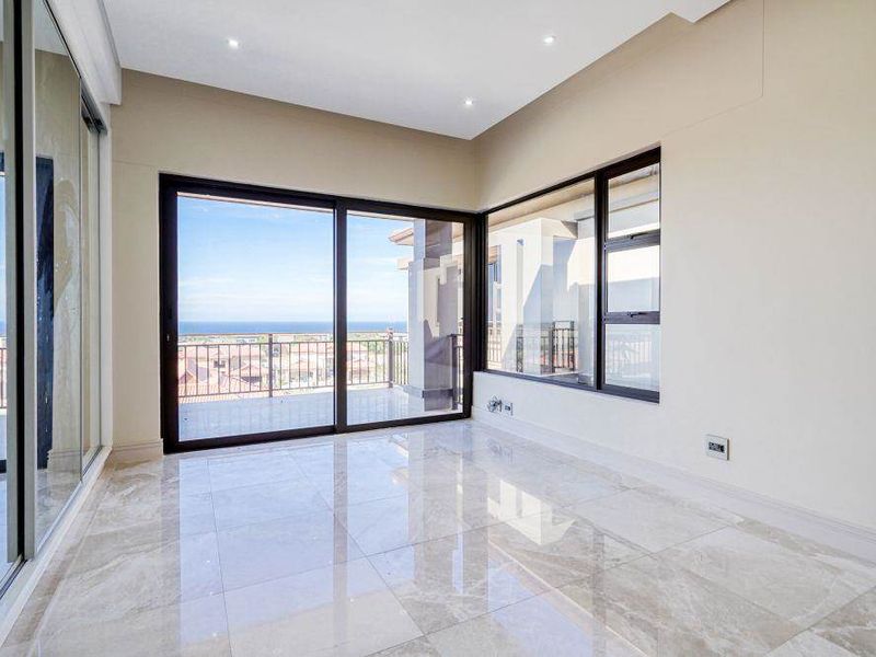 Bright and spacious living area featuring large sliding glass doors, expansive windows, and polished marble-look floor tiles with a scenic coastal view.
