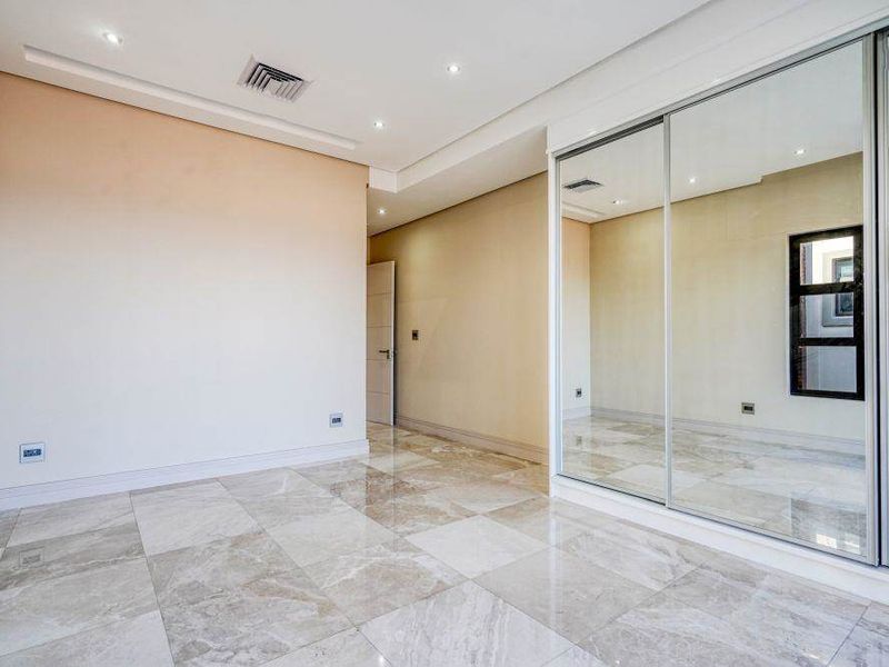 A bright, modern bedroom featuring high-quality marble-look floor tiles, recessed lighting, and a large built-in mirrored sliding wardrobe.
