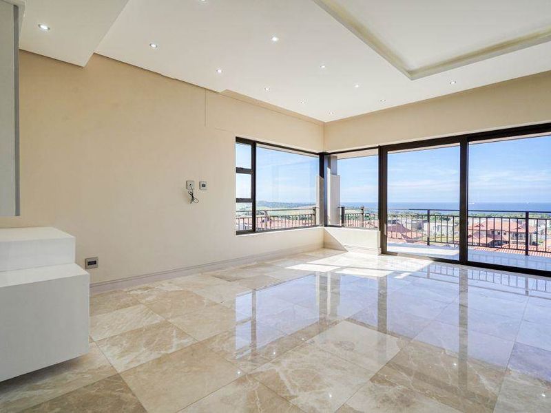 Spacious, light-filled living area featuring polished marble flooring, a modern coffered ceiling with recessed lighting, and expansive sliding doors opening to a balcony with views.