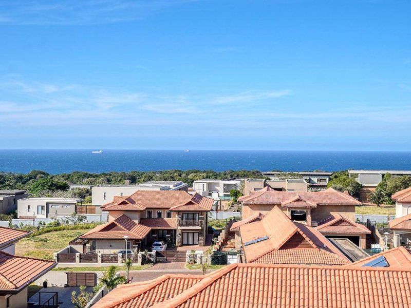 Elevated aerial view showcasing the surrounding residential estate with terracotta tiled roofs and a clear horizon view of the ocean.