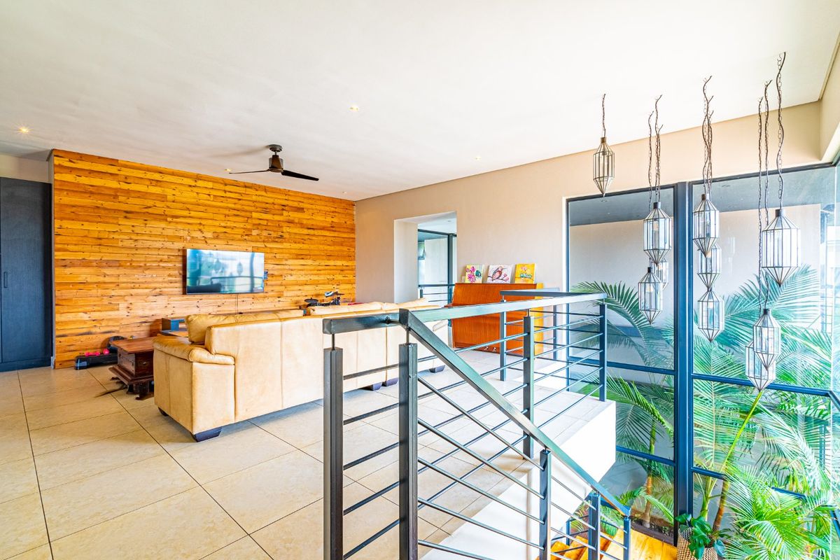 Spacious living area featuring a warm timber feature wall, tiled flooring, and a modern staircase with metal railings overlooking a bright indoor garden space.