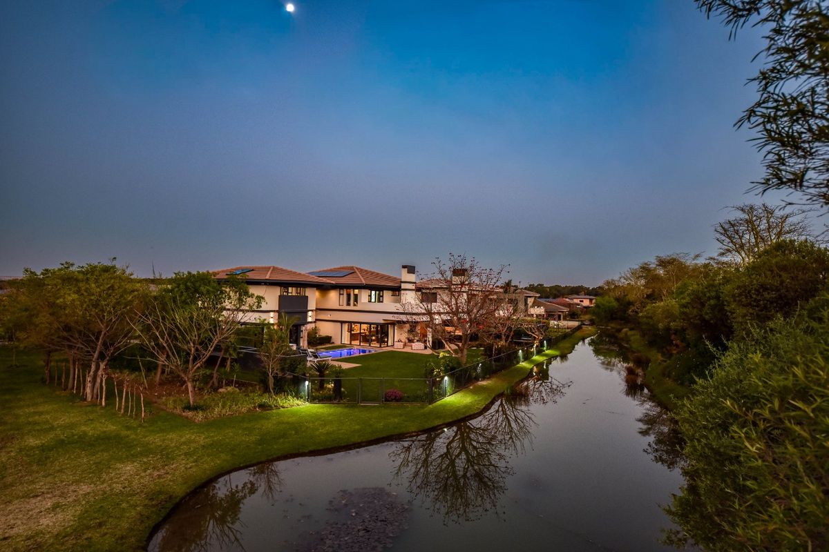 Aerial view of a luxury residence featuring a landscaped garden, swimming pool, and solar panels, situated along a scenic waterway at twilight.