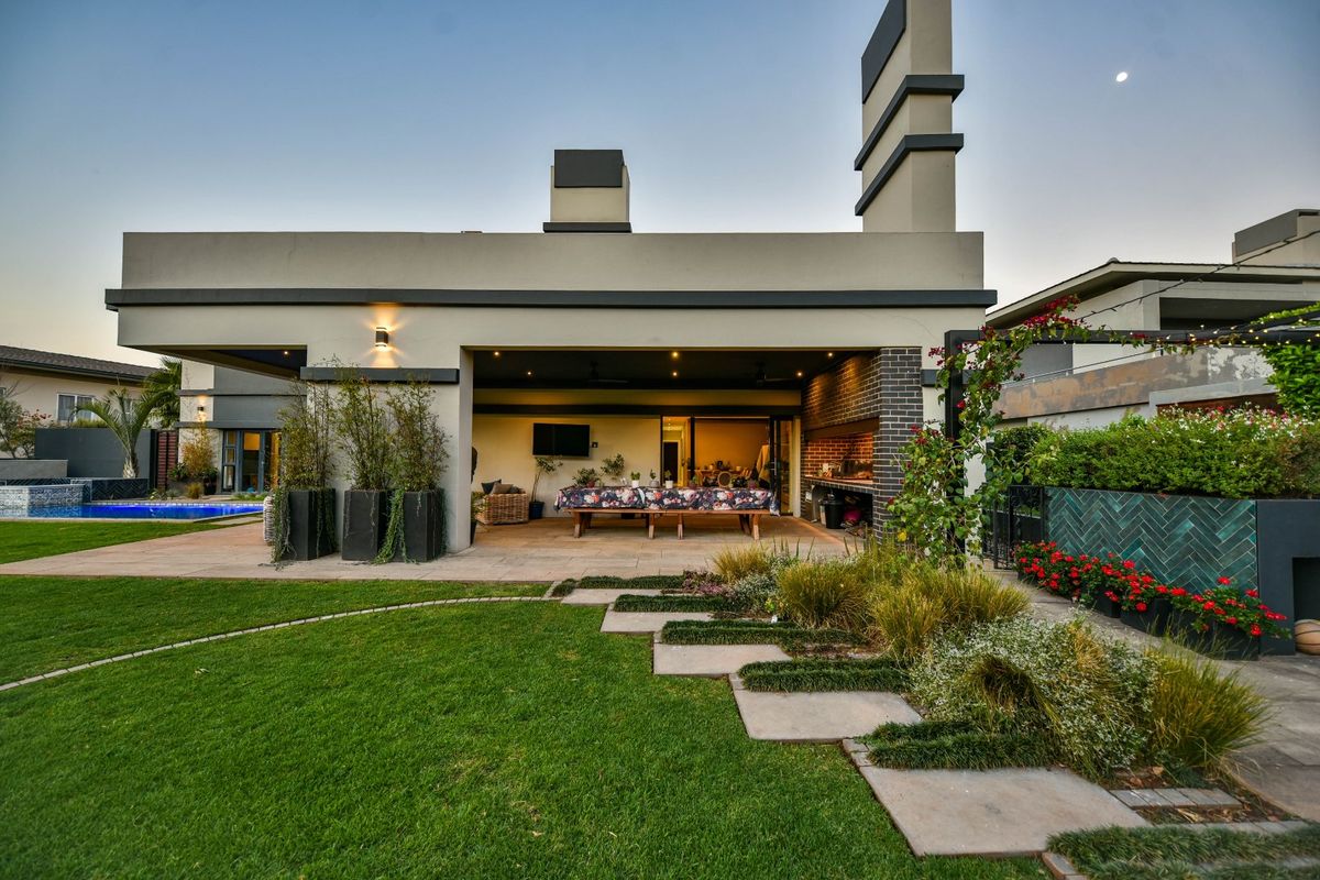 A well-maintained rear exterior featuring a spacious covered patio with a built-in braai, overlooking a landscaped garden and swimming pool.