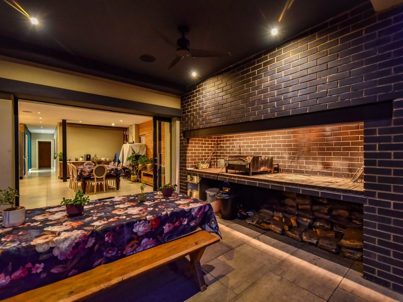 Covered outdoor patio featuring a large built-in brick braai, recessed lighting, and seamless flow into the interior dining area through sliding glass doors.