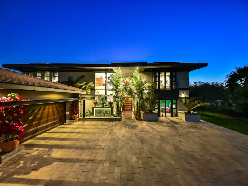 Stunning modern double-story residence featuring a spacious paved driveway, integrated double garage, and an elegant entrance with a built-in water feature at dusk.