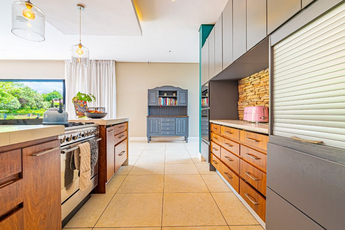 Modern kitchen featuring wood-finish cabinetry, stone tile flooring, a stone-clad backsplash, and integrated appliances with contemporary pendant lighting.