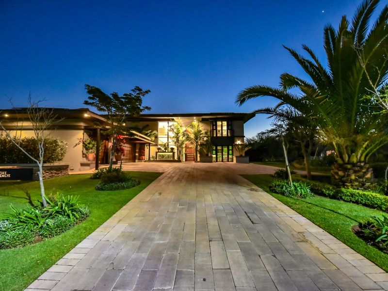 A stunning evening view of the property's front facade, featuring a paved driveway, manicured landscaping, and elegant exterior lighting.
