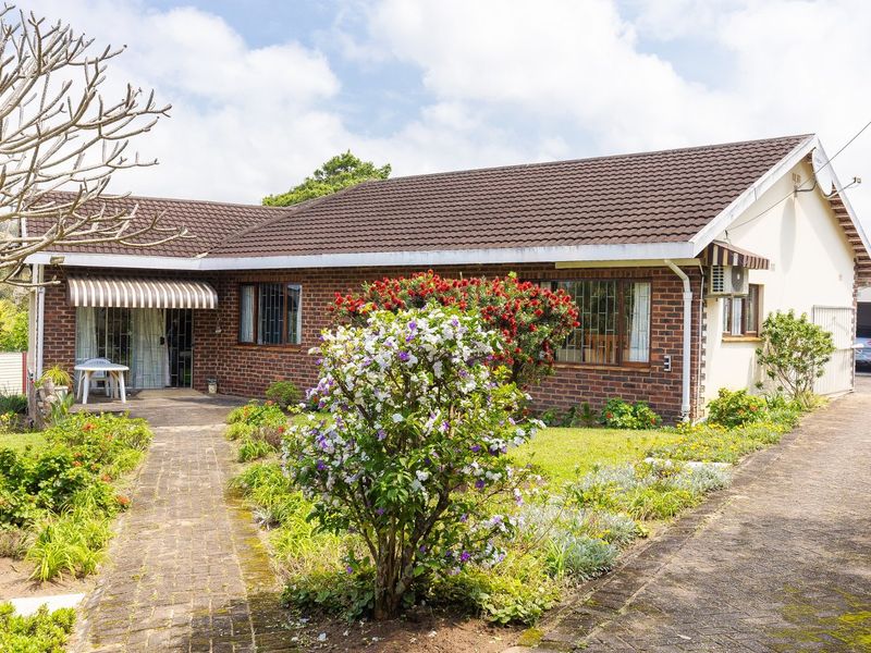 A well-maintained single-story brick house featuring a tiled roof, paved driveway, and established garden with mature landscaping.
