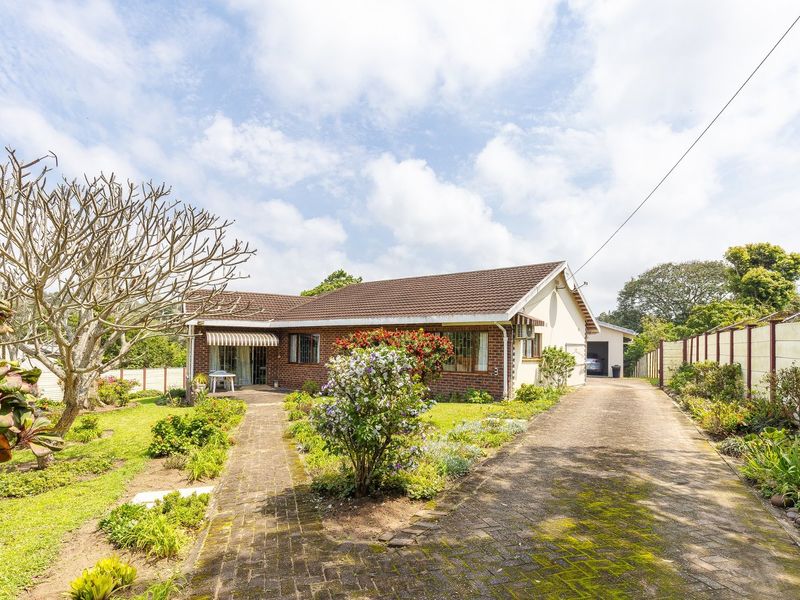 Front view of a single-story brick house featuring a tiled roof, paved driveway, established garden, and a covered patio area.