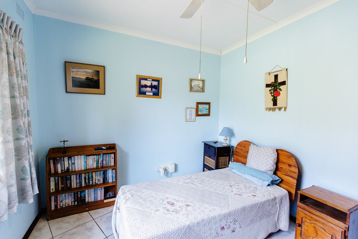 A functional bedroom featuring light blue walls, tiled flooring, and a ceiling fan, offering a clean and well-maintained space.