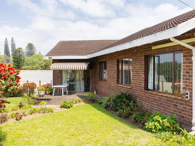 Rear view of a brick house featuring a concrete patio, striped awning, and established garden area with mature landscaping.