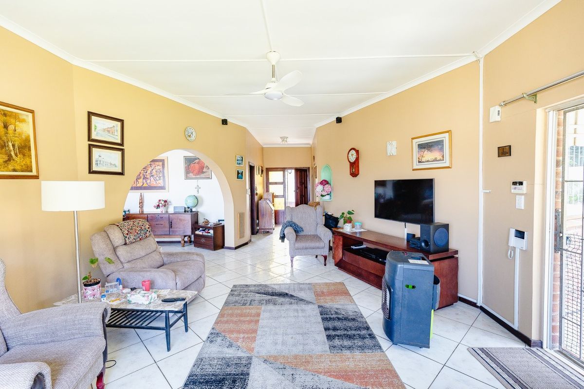 A spacious living room featuring tiled flooring, a ceiling fan, and an arched entryway leading to adjacent living areas with access to the outdoors.