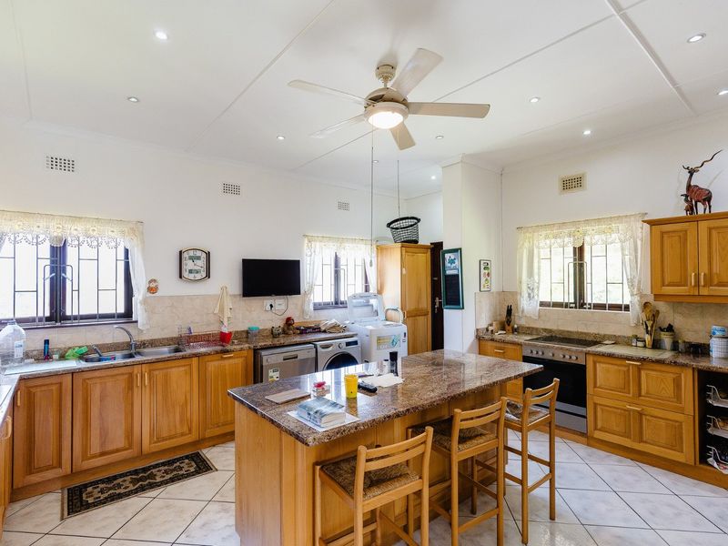 Spacious kitchen featuring wooden cabinetry, granite countertops, a central island, and tiled flooring, offering a functional layout with ample storage and workspace.